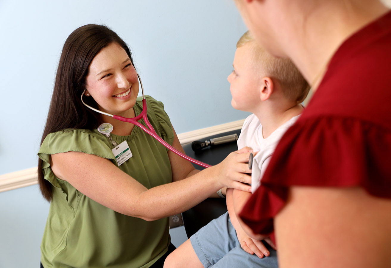 A smiling pediatric doctor listening to a child's heartbeat.