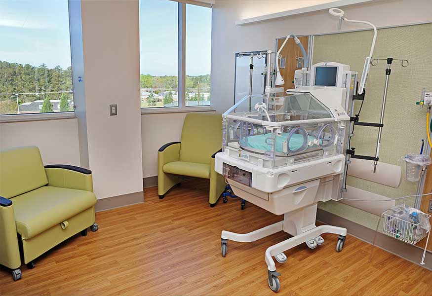 A delivery suite with a neonatal incubator and chairs in the room.